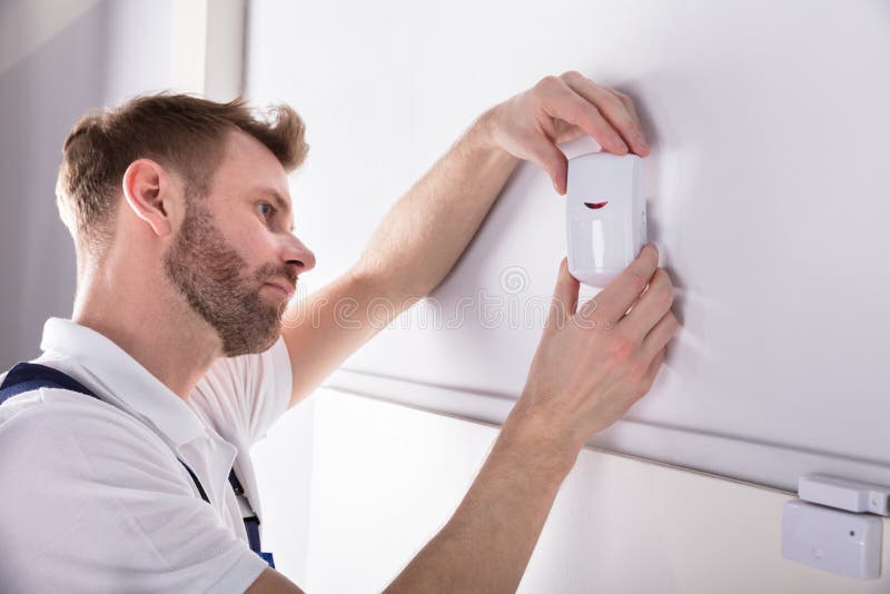 Close-up Of Young Male Electrician Installing Security System Door Sensor On Wall. Close-up Of Young Male Electrician Installing Security System Door Sensor On Wall