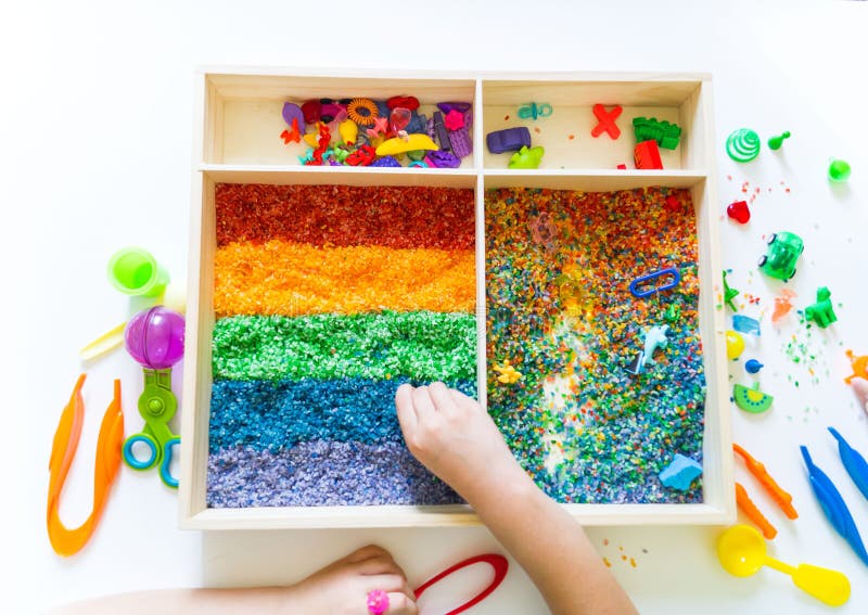 Sensory box with rainbow rice inside. Montessori material baby