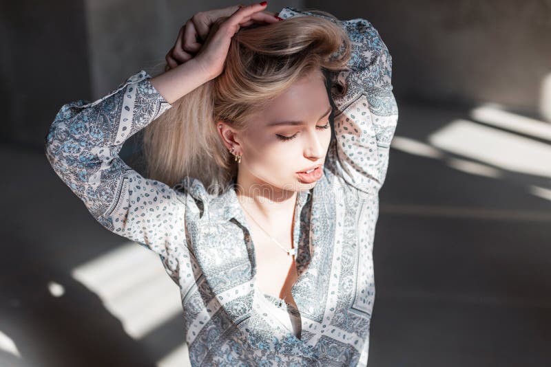 Sensual beautiful cute young blond woman with sexy lips with natural make-up in a vintage shirt with a pattern in the studio. Attractive girl fashion model enjoys bright sunshine