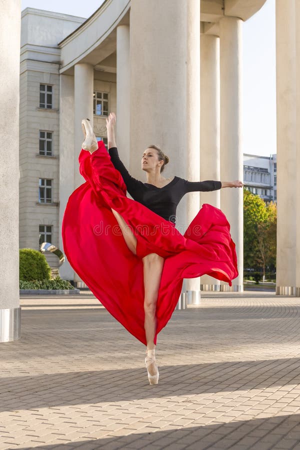 Sensual winsome exprescasian ballet dancer in red dress klädd in red skirt medan i dansställning med upplysta händer mot royaltyfria bilder