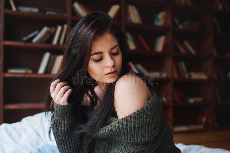 Sensual woman with dark hair in green sweater and jeans sitting on a bed royalty free stock photography Sensual woman with dark hair in green sweater and jeans sitting on a bed royalty free stock photography