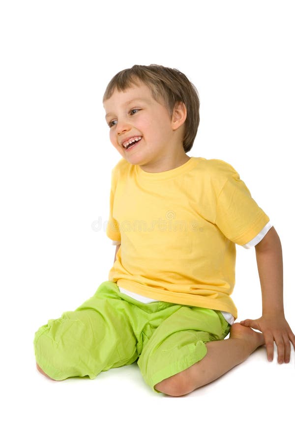 Young boy smiles widely while sitting with legs tucked behind him. Model is dressed in yellow and green summer weight clothing. Isolated on white. Young boy smiles widely while sitting with legs tucked behind him. Model is dressed in yellow and green summer weight clothing. Isolated on white.