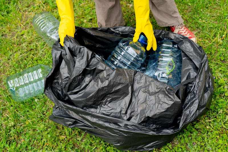 Hands in yellow gloves putting big plastic bottles into bllack plastic trash bag