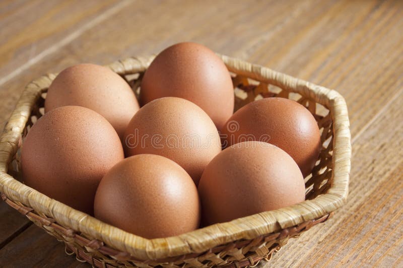 Sept oeufs bruns de poulet s'étendent dans un panier en osier sur une table image stock Sept oeufs bruns de poulet s'étendent dans un panier en osier sur une table image stock