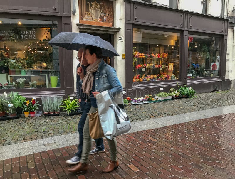 Couple under umbrella strolls past Antwerp flower shop in the ra