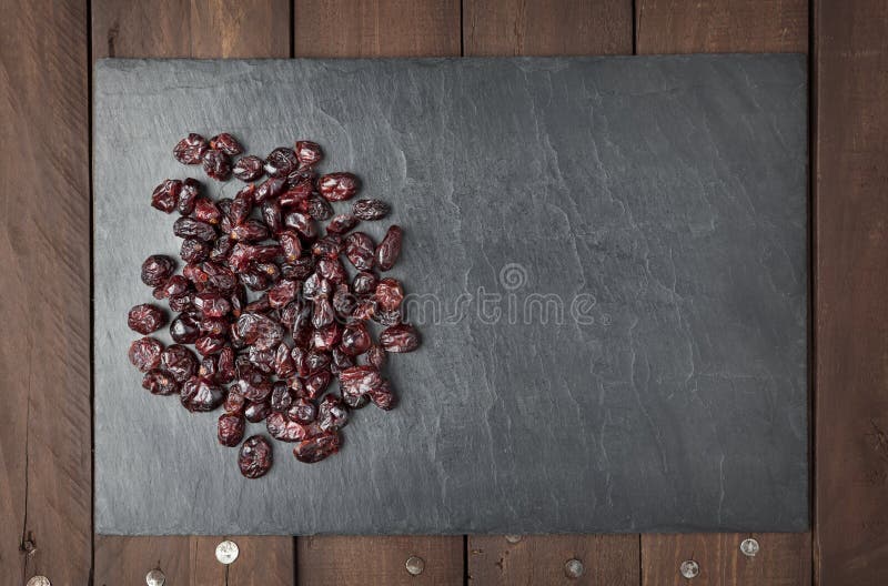 Dry red cranberries on a square shaped slate plate on a brown wooden table. Copy space. Dry red cranberries on a square shaped slate plate on a brown wooden table. Copy space.