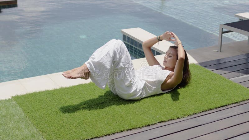 Calm wpman practicing yoga in balancing asana poolside against town on coast