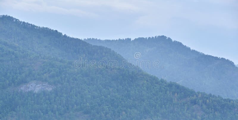 Serene mountain landscape with lush green forests and soft blue sky in a misty stock images