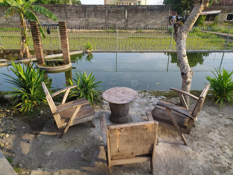 A serene outdoor setting features three rustic wooden chairs and a round table stock photo