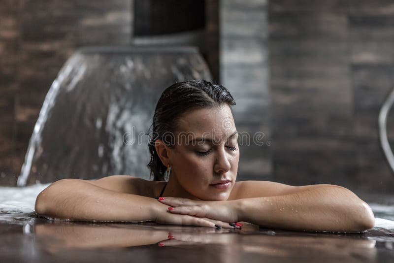 Tranquil young female with wet hair enjoying relaxing hydrotherapy session in spa pool with waterfall jet while spending time in luxury wellness center. Tranquil young female with wet hair enjoying relaxing hydrotherapy session in spa pool with waterfall jet while spending time in luxury wellness center