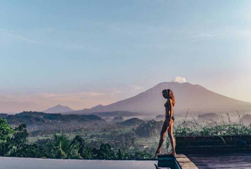 Beautiful girl staying near swimming pool with fantastic volcano