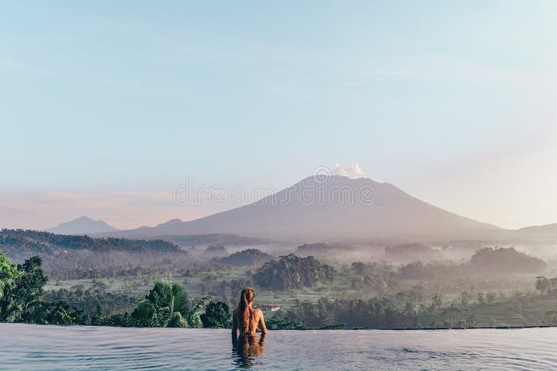 Beautiful girl staying near swimming pool with fantastic volcano