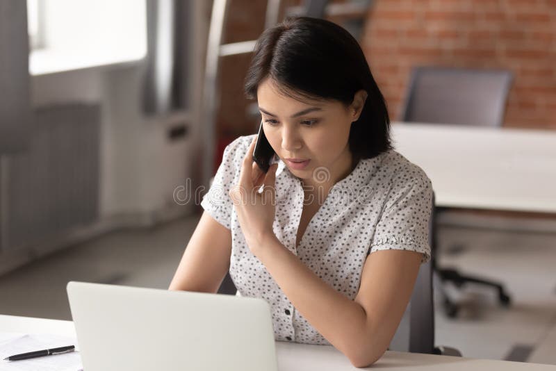 Serious asian businesswoman using laptop talking on phone in office