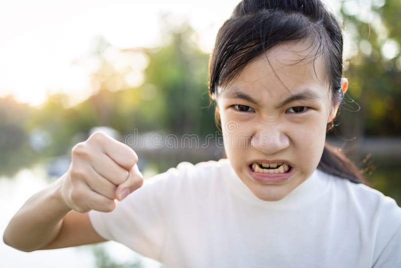 Serious asian child girl with her fist raised for threat warning or quarreling,angry female threatening with fist,about to punch,aggressive schoolgirl,facial expression,concept of aggression,bully