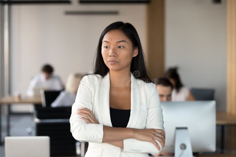 Serious asian female employee standing in coworking office and t