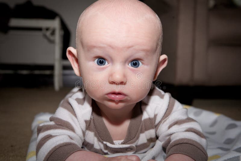 Baby with blue eyes with a serious expression lying on his stomach with drool hanging from his mouth. Image orientation is horizontal and there is copy space. Baby with blue eyes with a serious expression lying on his stomach with drool hanging from his mouth. Image orientation is horizontal and there is copy space.