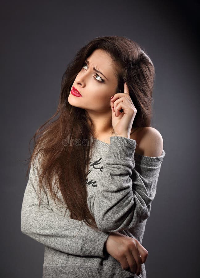 Serious beautiful woman in casual clothing looking up and thinking on dark grey background with empty copy space