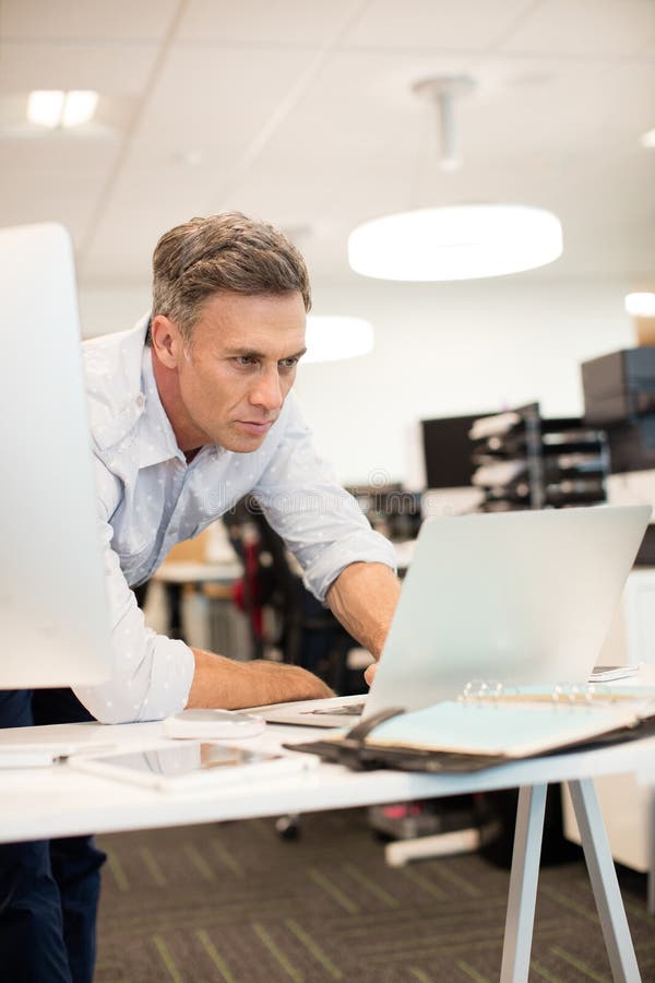 Serious Businessman Looking at Laptop while Leaning on Desk Stock Photo Image of elegant