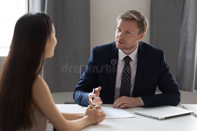 Serious businessman talk with female job candidate at interview. Serious businessman sit at office desk talk interview young women work candidate in office royalty free stock photography Serious businessman talk with female job candidate at interview. Serious businessman sit at office desk talk interview young women work candidate in office royalty free stock photography
