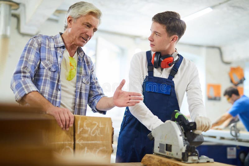 Serious carpenter giving advice to intern in workshop stock photo Serious carpenter giving advice to intern in workshop stock photo