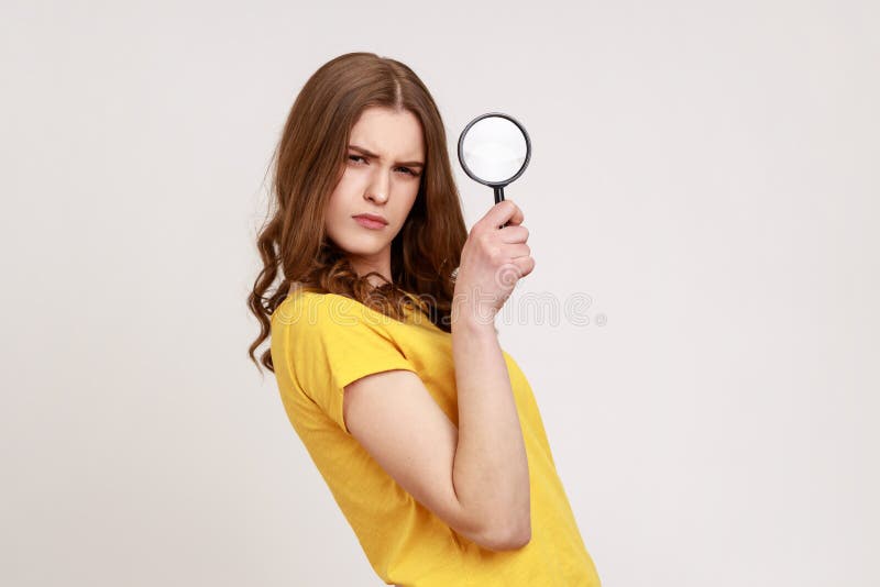 Serious confident teenager girl detective in casual style yellow t-shirt holding in hand magnifying