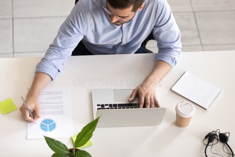 Serious employee using laptop, making notes, top view stock images Serious employee using laptop, making notes, top view stock images