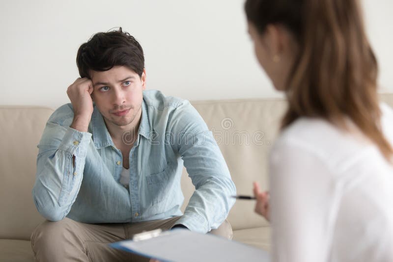 Joven grave hombres sobre el sofá escuchando con cuidado sobre el consejo de Un psicólogo, o, discusión médico los resultados, explicación diagnóstico, tratamiento métodos.