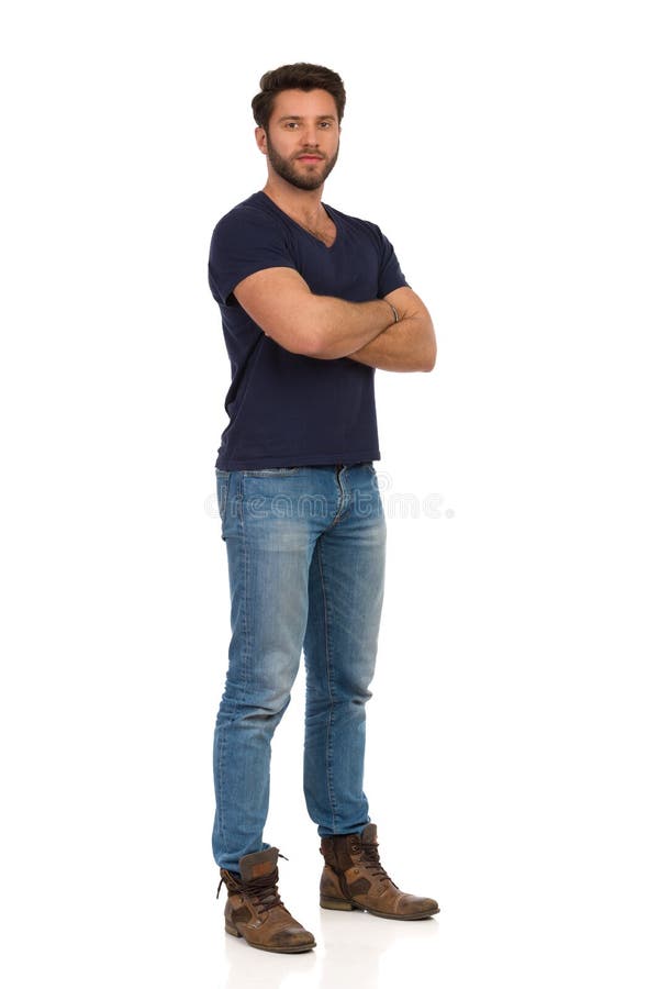 Serious Handsome Man In Boots, Jeans And Blue T-shirt Is Standing With Arms Crossed
