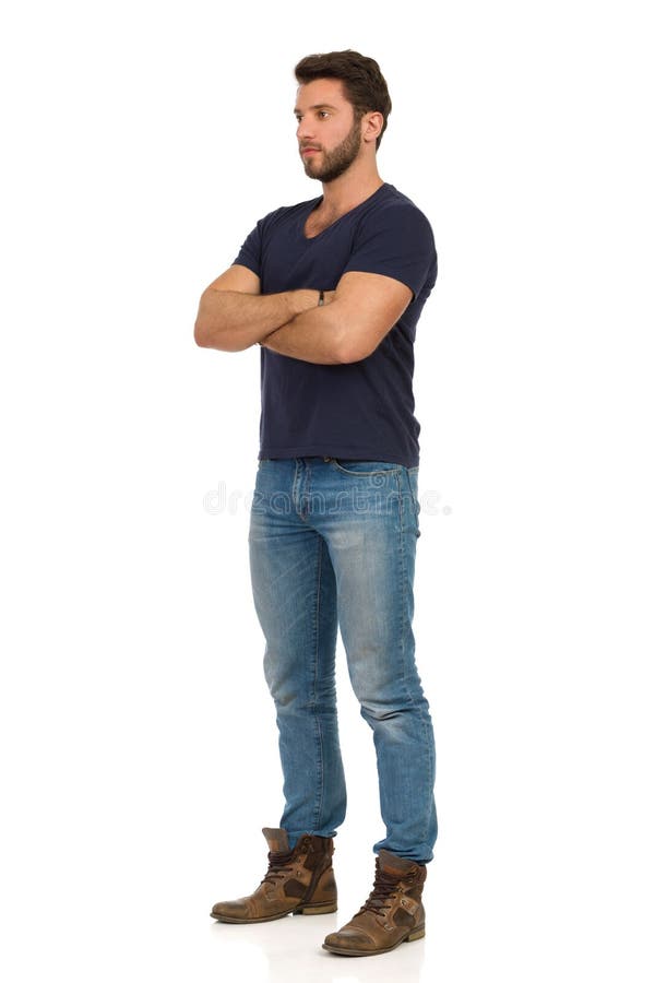 Serious Handsome Man In Jeans, Boots And Blue T-shirt Is Standing With Arms Crossed