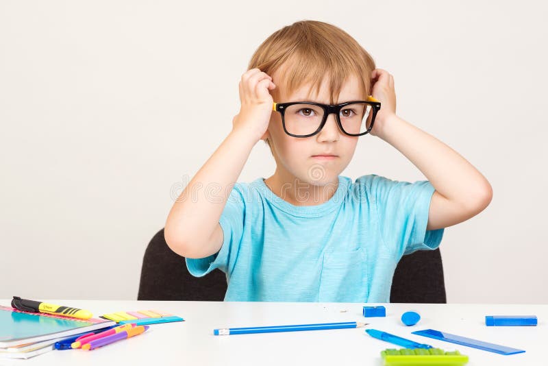 Serious kid in eyeglasses is sitting at a desk. Little child writing with colorful pencils, indoors. Elementary school and stock photos Serious kid in eyeglasses is sitting at a desk. Little child writing with colorful pencils, indoors. Elementary school and stock photos