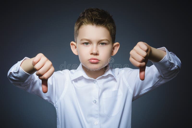 Serious little boy holding his thumb down on gray background royalty free stock photography Serious little boy holding his thumb down on gray background royalty free stock photography