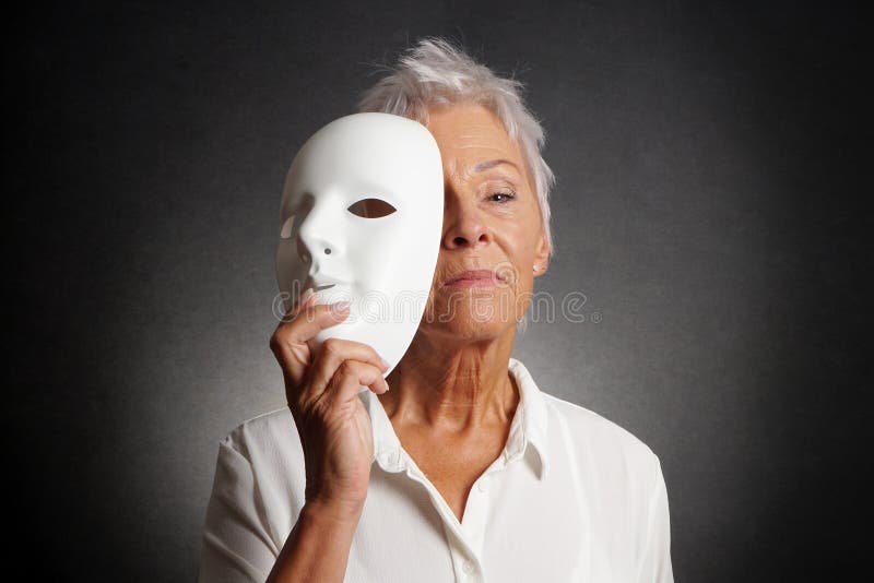 Serious older woman revealing face behind mask stock photos