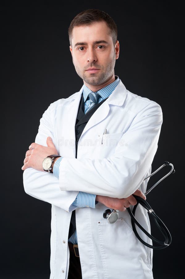 Serious male doctor holds stethoscope in hand isolated on black