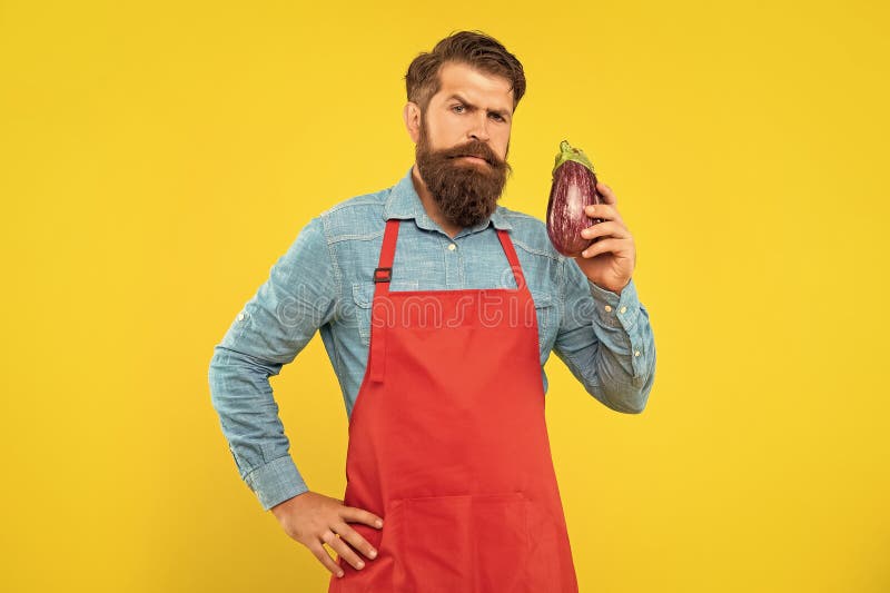 Serious man in apron holding eggplant yellow background, grocer royalty free stock photos