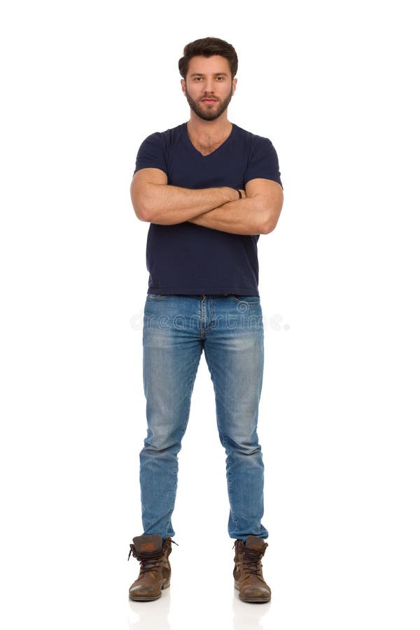 Serious Man In Boots, Jeans And Blue T-shirt Is Standing With Arms Crossed