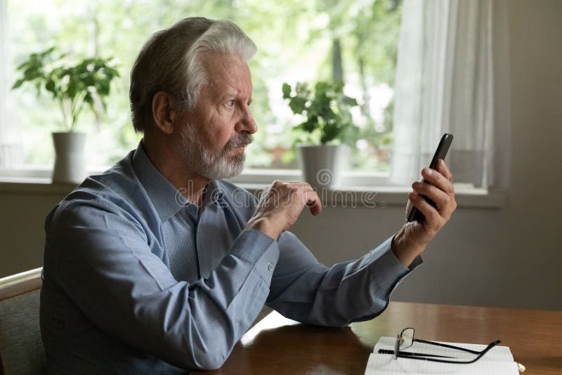 Serious mature smartphone user reading message on screen