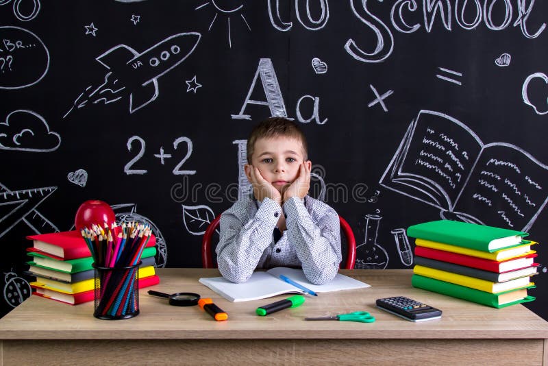 Serious schoolboy sitting on the desk with books, school supplies, with both arms under the cheecks stock images Serious schoolboy sitting on the desk with books, school supplies, with both arms under the cheecks stock images