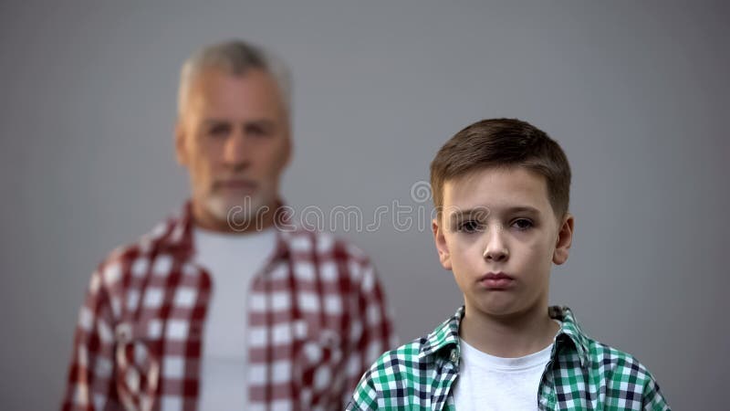 Serious teen boy looking at camera, aged male behind, connection with ancestors stock photo Serious teen boy looking at camera, aged male behind, connection with ancestors stock photo