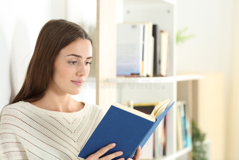 Serious teen reading a paper book standing at home