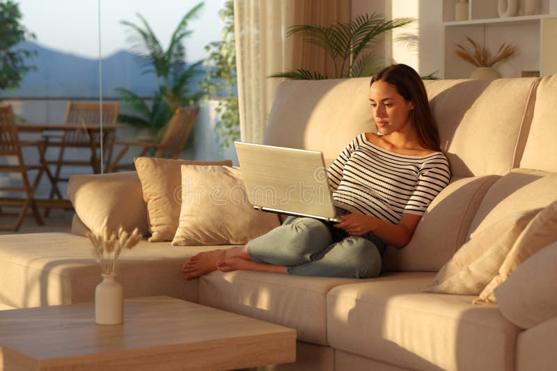 Serious woman sitting on a couch at home using personal computer at sunset. Laptop personal computer stock images, royalty-free photos and pictures
