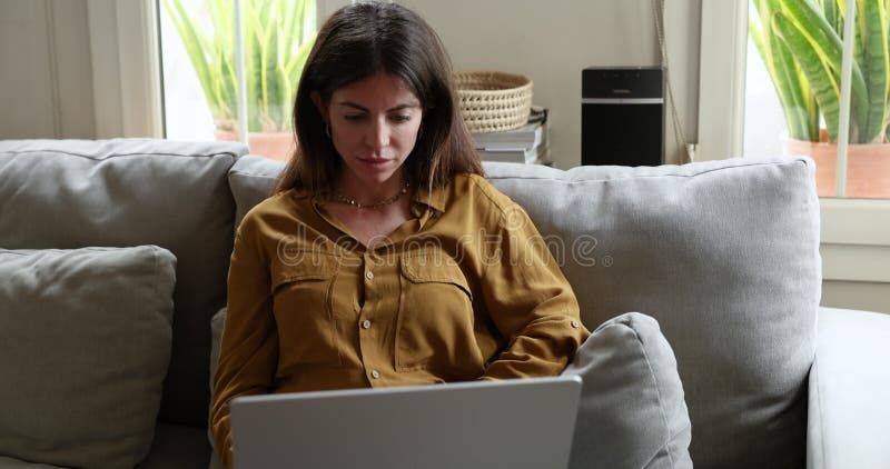 Serious woman using laptop sit on sofa in living room stock video