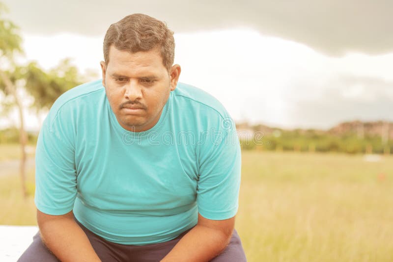 Seriously fat man on outdoor, park - concept of sadness due overweight - Indian obese man feeling unhappy or depressed.