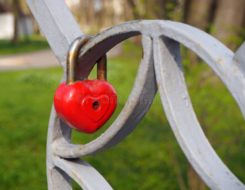 Serratura rossa del cuore del metallo arrugginito vecchio, il simbolo romantico di amore senza fine che appende sul recinto del p fotografia stock Serratura rossa del cuore del metallo arrugginito vecchio, il simbolo romantico di amore senza fine che appende sul recinto del p fotografia stock