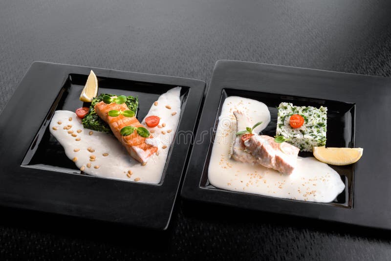 Servant à un plat le filet saumoné à une sauce crémeuse avec les épinards, le citron et les pousses du soja d'un plat noir photo libre de droits Servant à un plat le filet saumoné à une sauce crémeuse avec les épinards, le citron et les pousses du soja d'un plat noir photo libre de droits