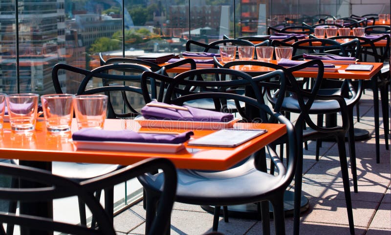 Interior of a modern restaurant with modern orange rectangular tables and chairs and a stylish serving in the attic outdoors behind a glass barrier against the backdrop of high-rise buildings of downtown Portland. Interior of a modern restaurant with modern orange rectangular tables and chairs and a stylish serving in the attic outdoors behind a glass barrier against the backdrop of high-rise buildings of downtown Portland.
