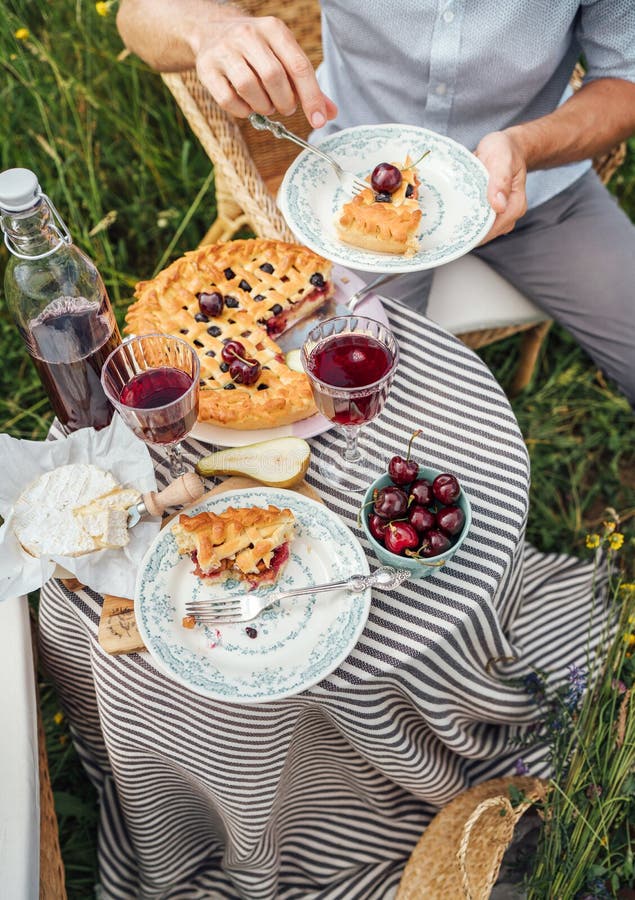 Served table top view with fruit pie and vintage tableware, red wine in glasses, man eating a tasty dessert,  sitting in rattan