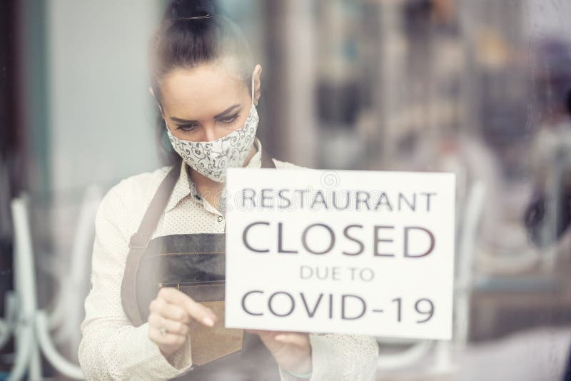 Serveerster tekent bord met de vermelding dat restaurant gesloten is vanwege covid19 op een raam