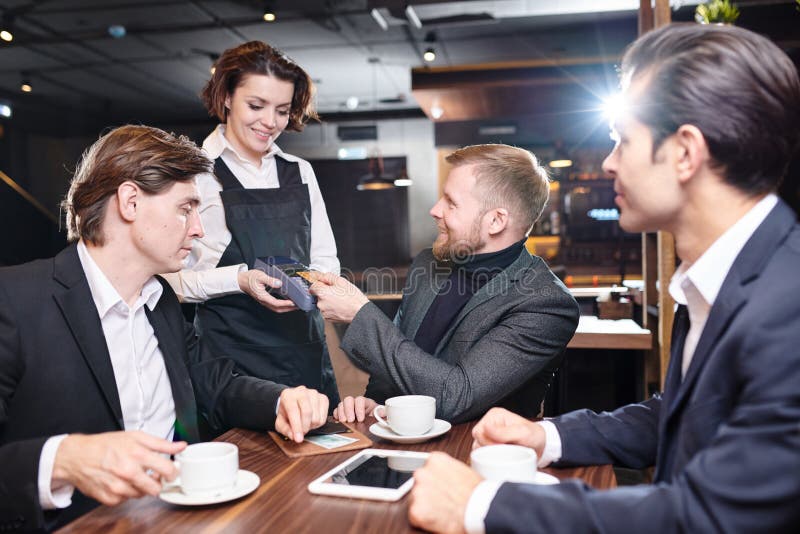 Serveuse positive donnant le terminal de paiement aux invités d'affaires dedans images stock Serveuse positive donnant le terminal de paiement aux invités d'affaires dedans images stock