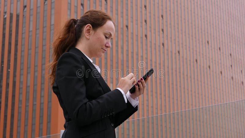 Service de mini-messages de femme d'affaires dans le smartphone au downown contre le gratte-ciel