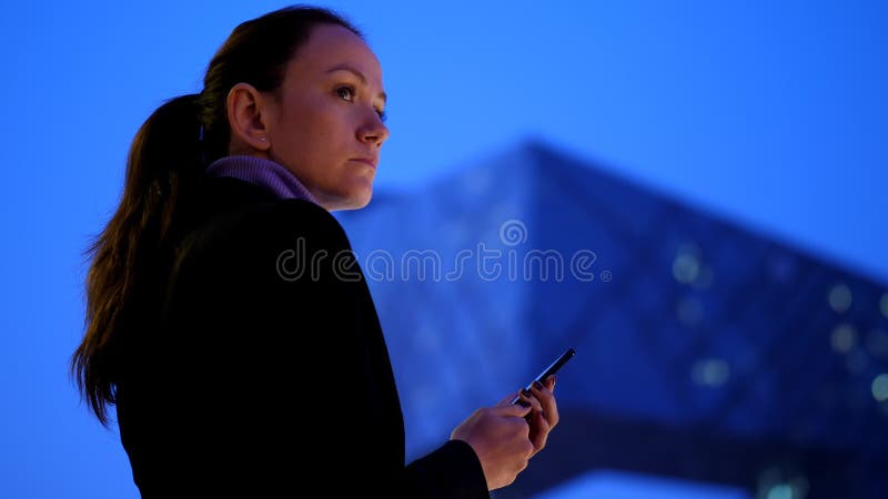 Service de mini-messages de femme dans le smartphone se tenant contre le paysage urbain moderne de nuit